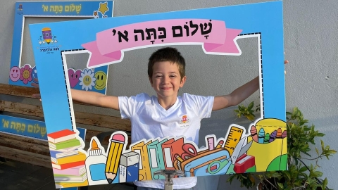 תלמיד מחזיק כרזה עם הכיתוב שלום כיתה א בפתיחת שנת הלימודים בכפר סבא